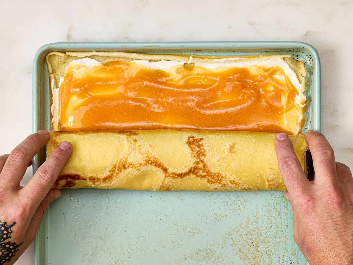 Hands rolling a filled crepe on a tray
