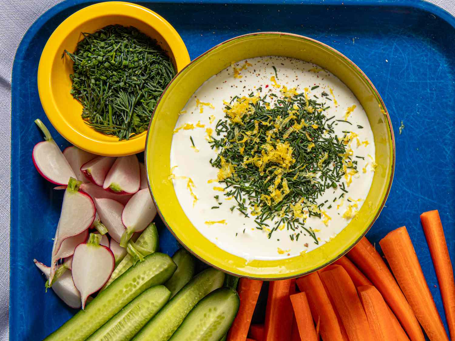 Whipped cottage cheese in a bowl with fresh herbs and lemon zest. Raw vegetables on the side.