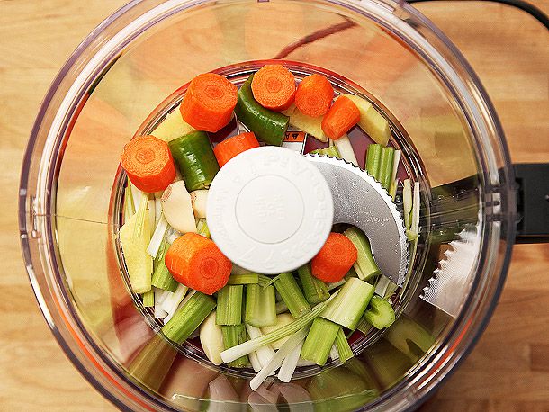 Overhead view of the bowl of a food processor containing chunks of carrot, celery, jalapeño, garlic, and ginger.
