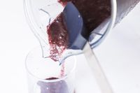 Using a metal and silicone spoon to scrape smoothie from the blender jar into a glass