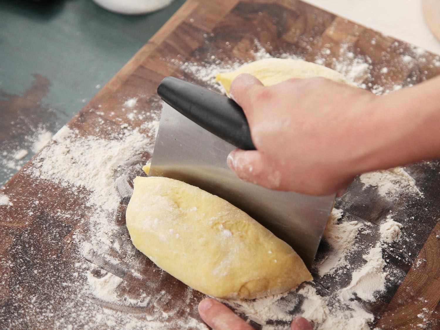 The cemita dough is cut in half with a bench scraper.