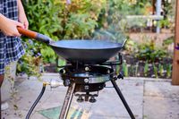 A person placing a wok onto an outdoor wok burner.