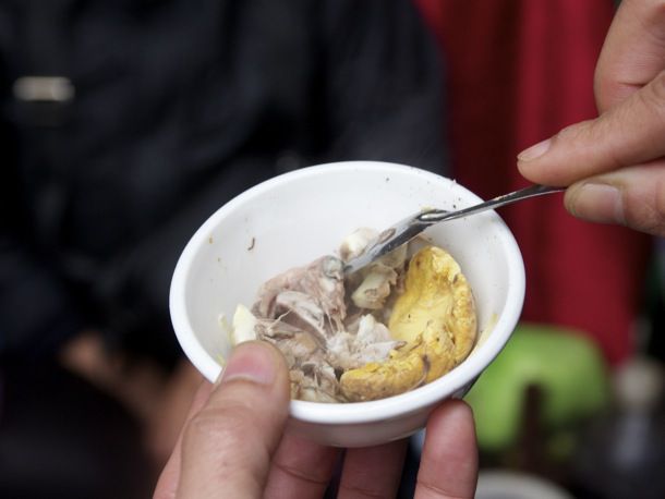 A spoon grabbing a bite of hot vit lon (Fetal Duck Eggs) from a small bowl