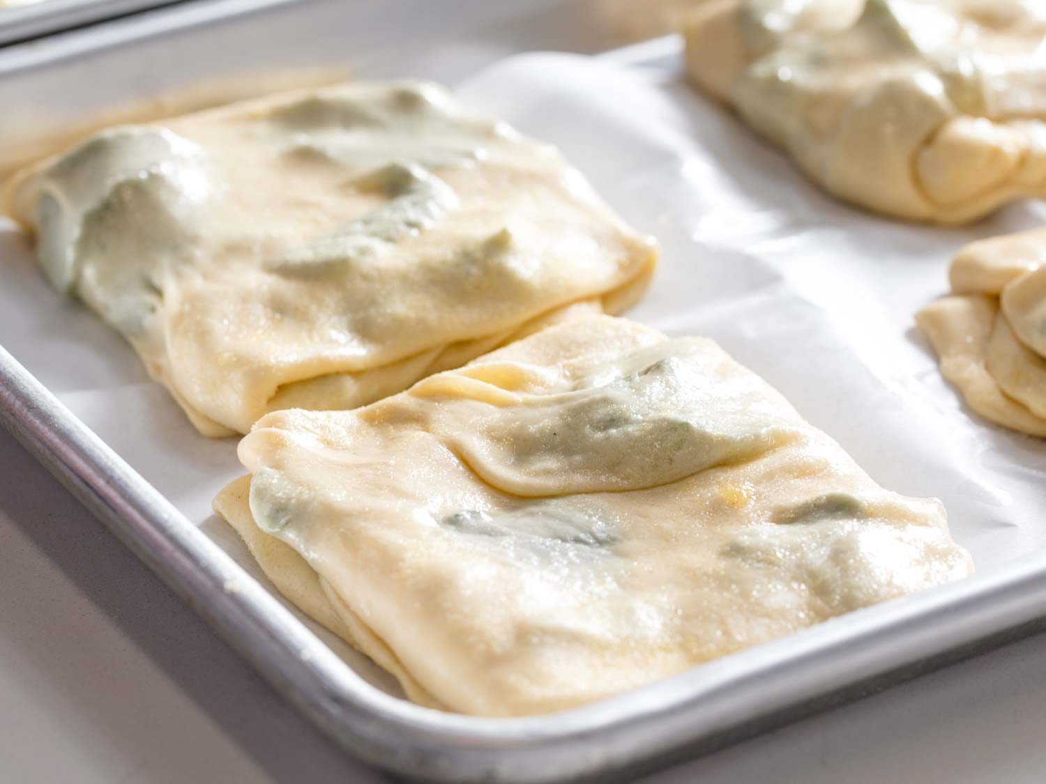 Squares of mint m'smen during second proofing on a rimmed baking sheet lined with parchment paper. 