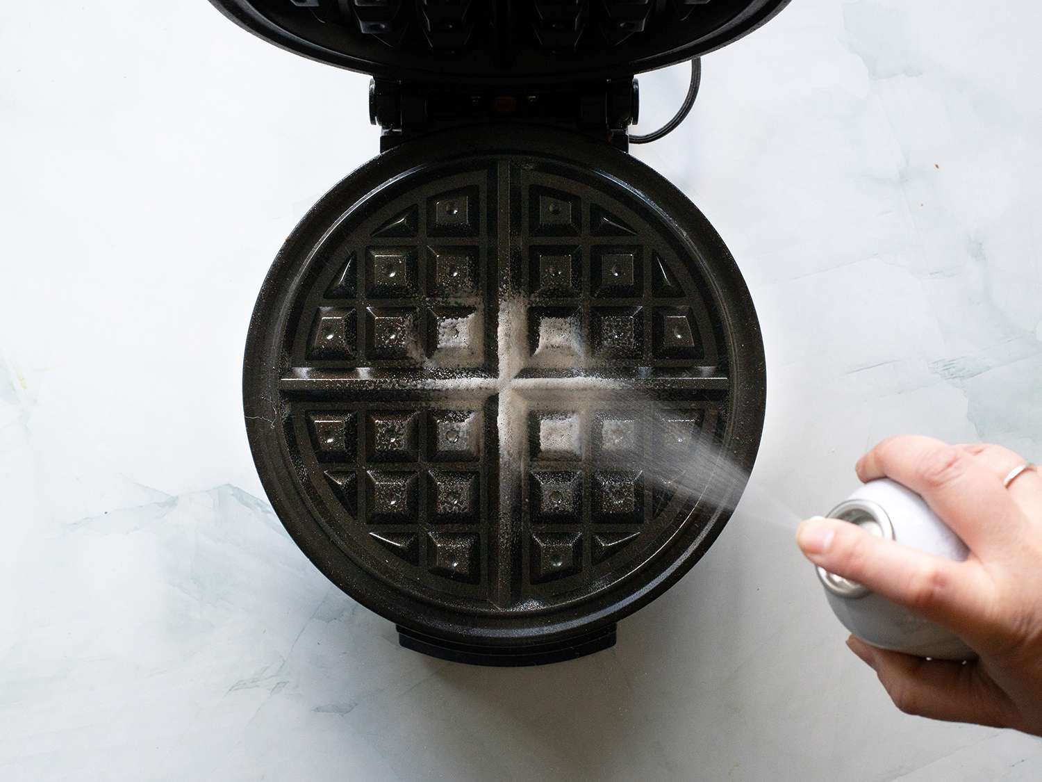 The waffle iron being coated with non-stick spray.