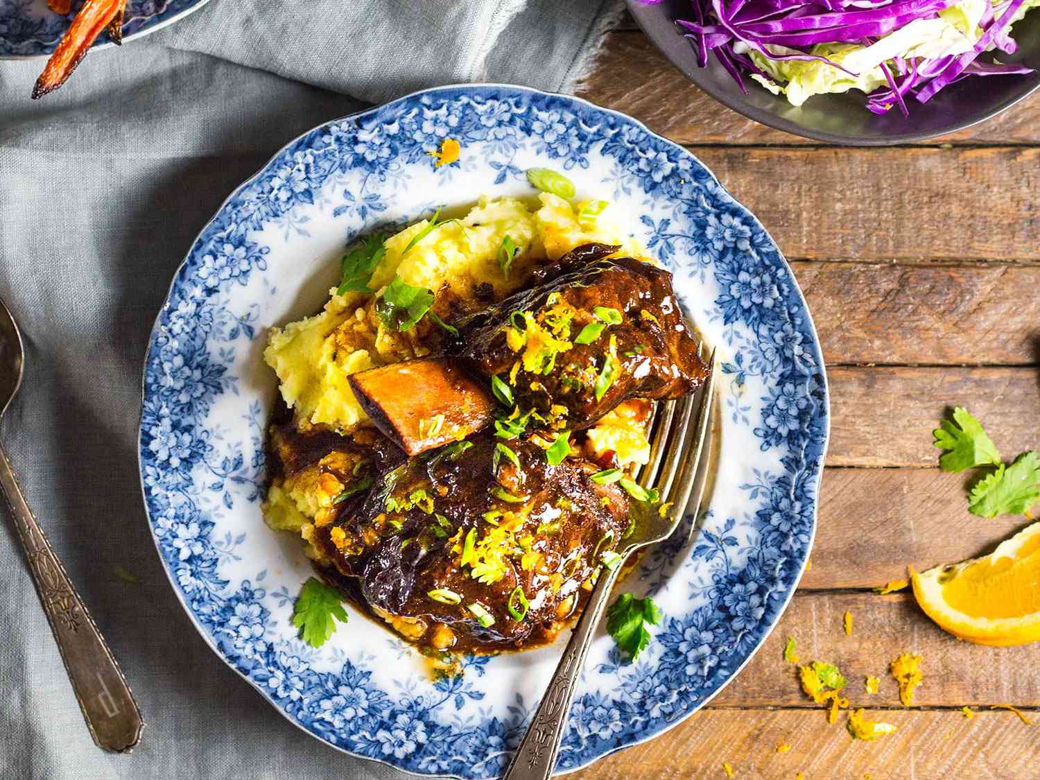Overhead photo of saucy braised short ribs dinner in blue and white bowl on a wooden table.