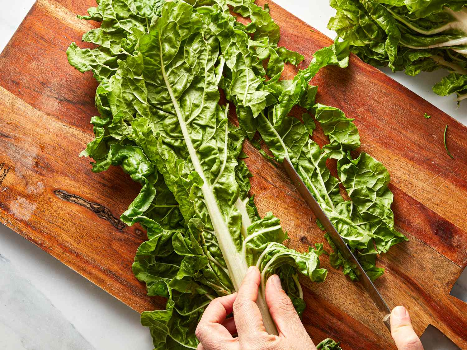 A person slicing leafy greens on a wooden cutting board