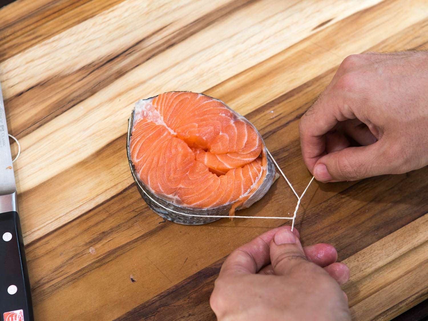 Tying up a salmon steak with an overhand knot with butcher's twine.