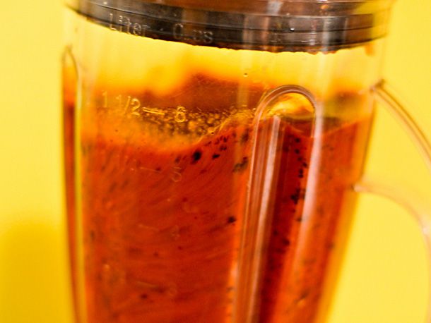 Pureeing chiles, garlic, tomatoes, cumin, and black pepper in jar of a blender for red enchilada sauce.