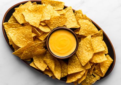 Nacho cheese sauce in a small bowl in the center of a platter, surrounded by tortilla chips.