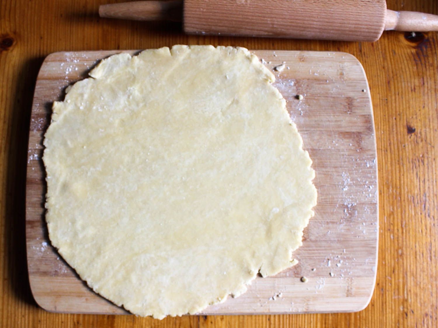 Pie dough has been rolled out on a cutting board.