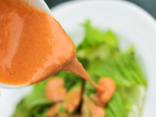 Close up view of creamy French dressing drizzling on a plate of lettuce.
