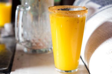 A rimmed pint glass of bright-orange pulque.