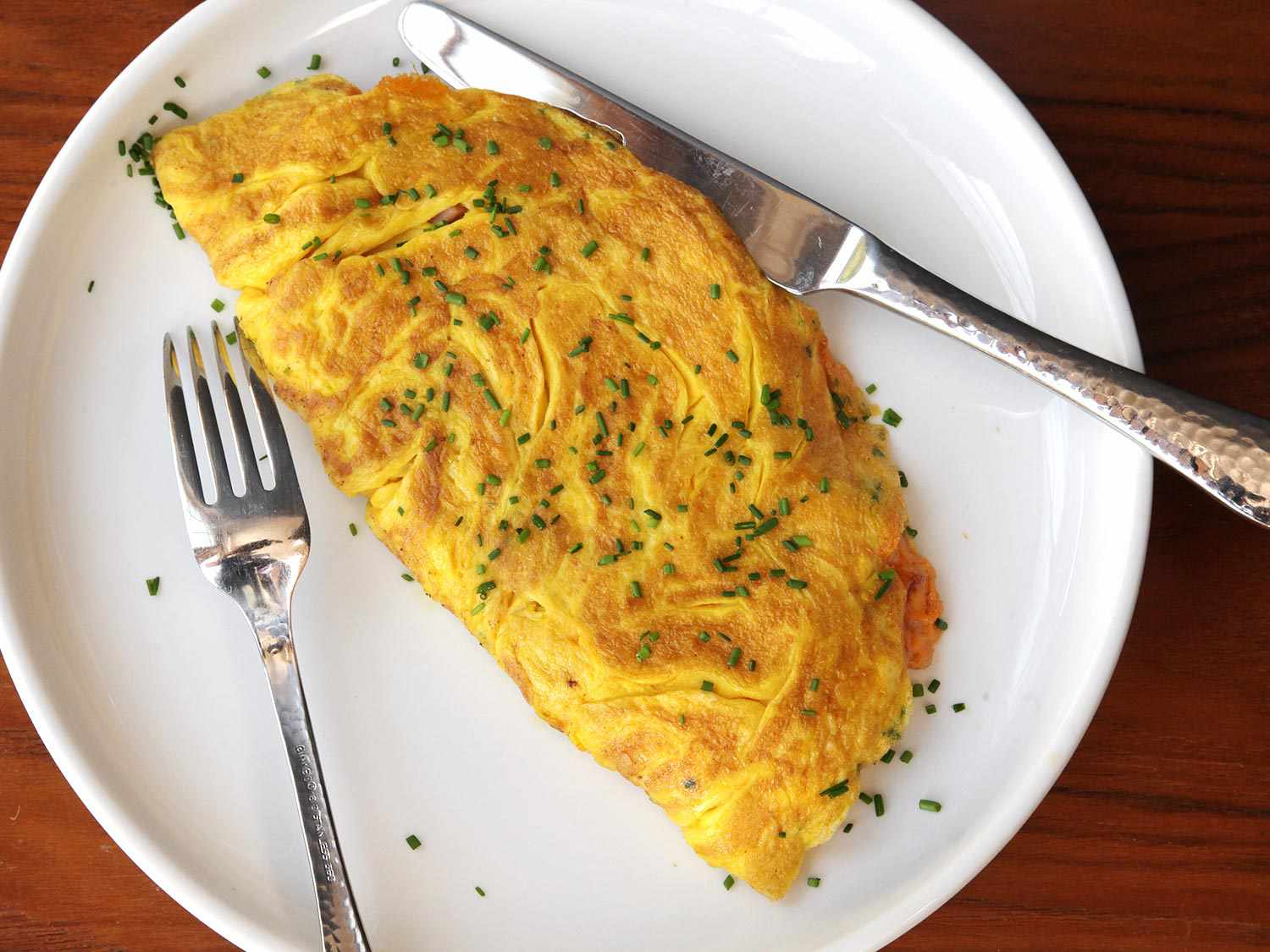 A fluffy, diner-style omelet topped with minced chives, on a white plate with silverware.