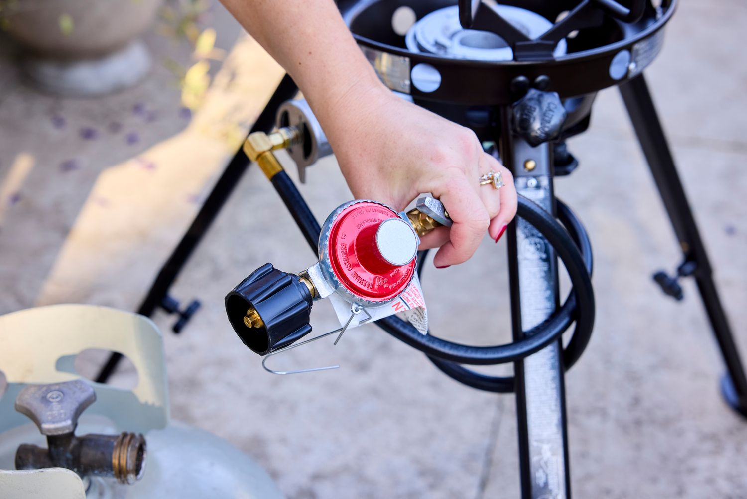 A person attaching a propane tank an outdoor wok burner.