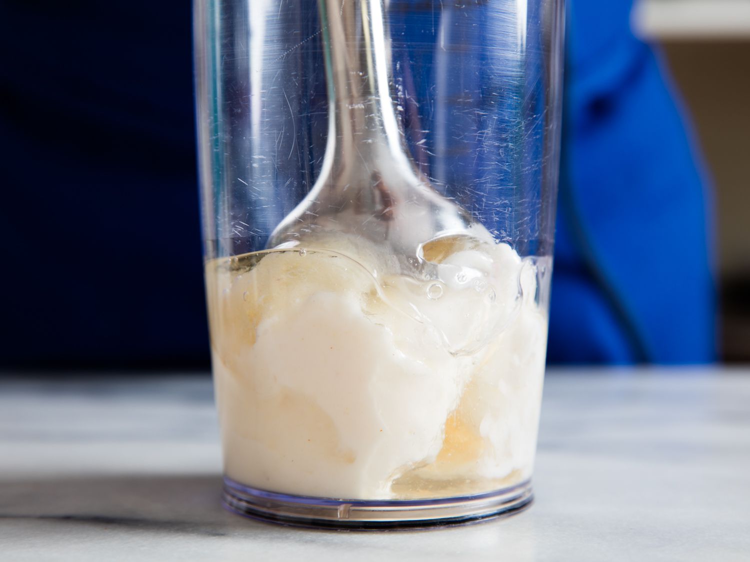 An immersion blender blending egg whites and oil in a jar. 