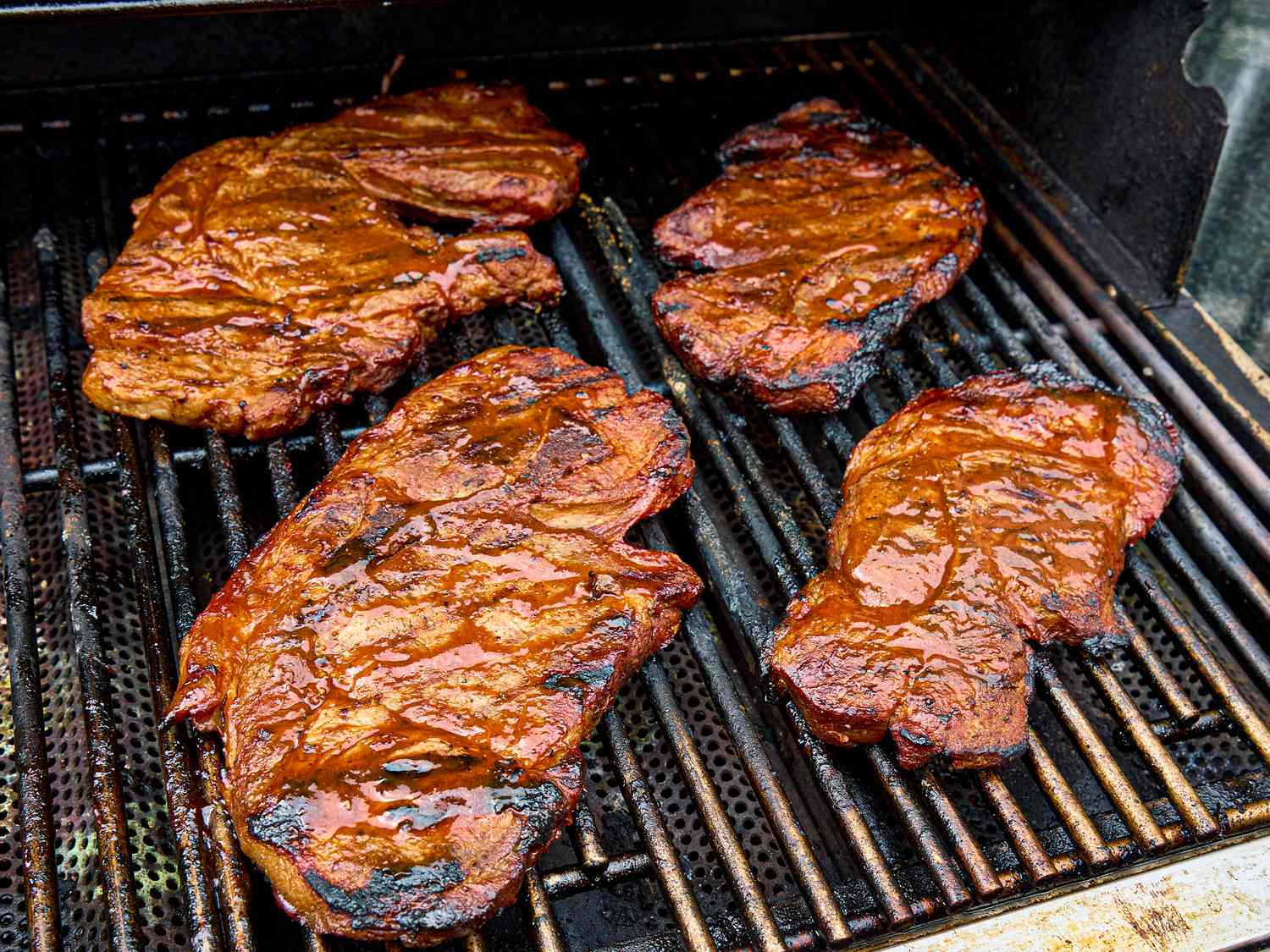 Four pork steaks cooking on a grill