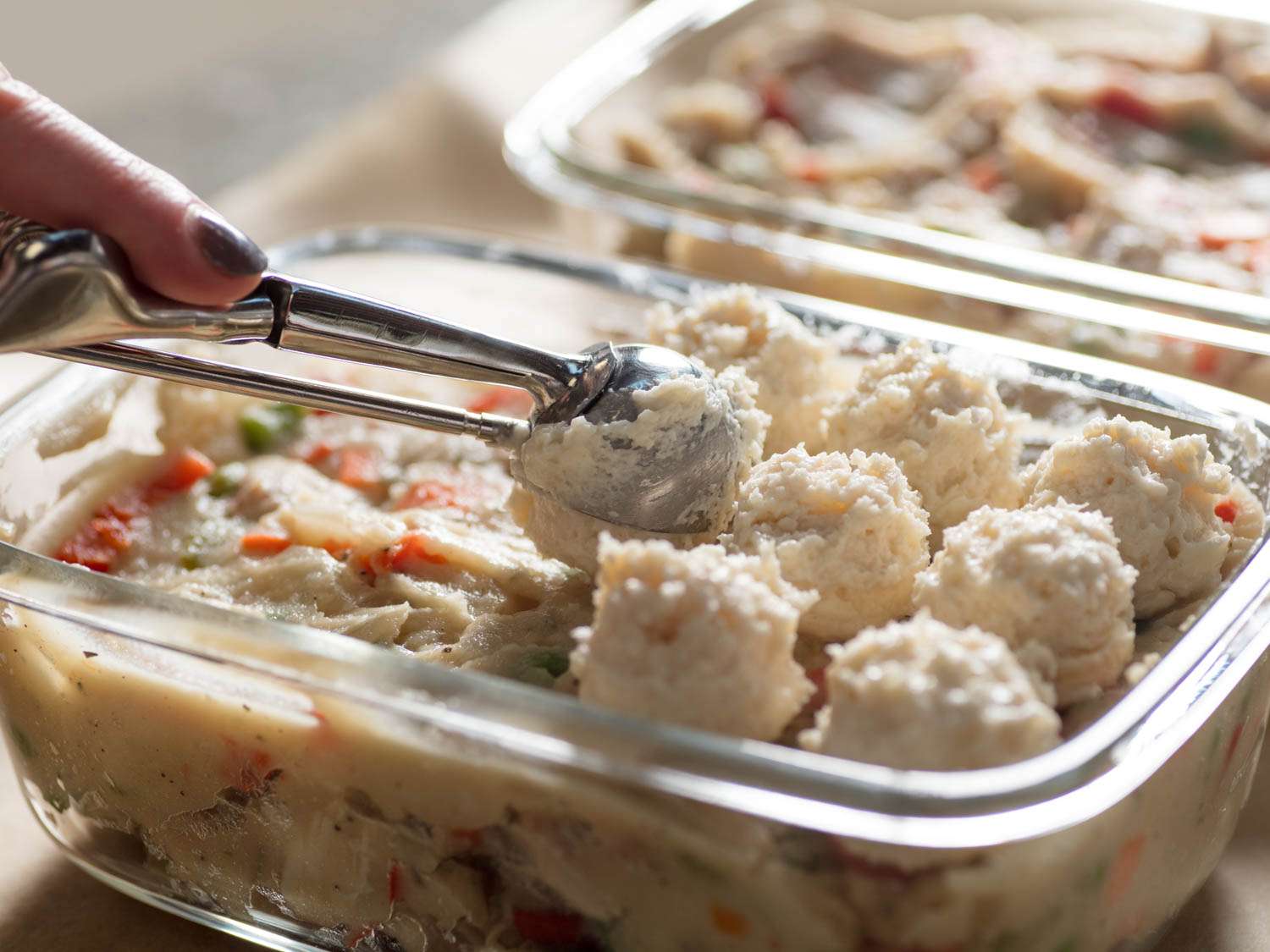 Scooping biscuit topping on top of chicken pot pie filling.