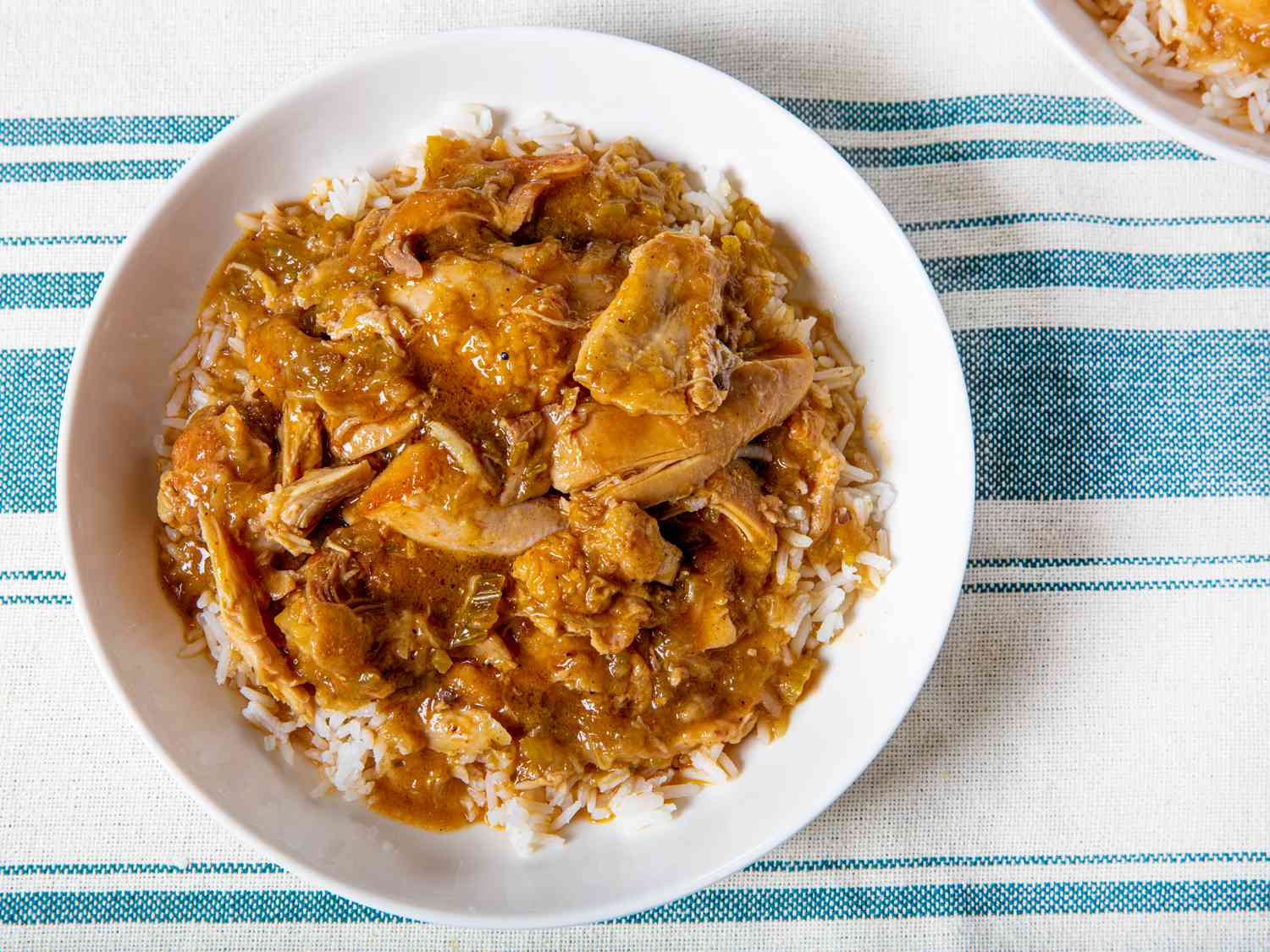 Overhead view of a bowl of lowcountry stew chicken over rice on a striped white and blue background