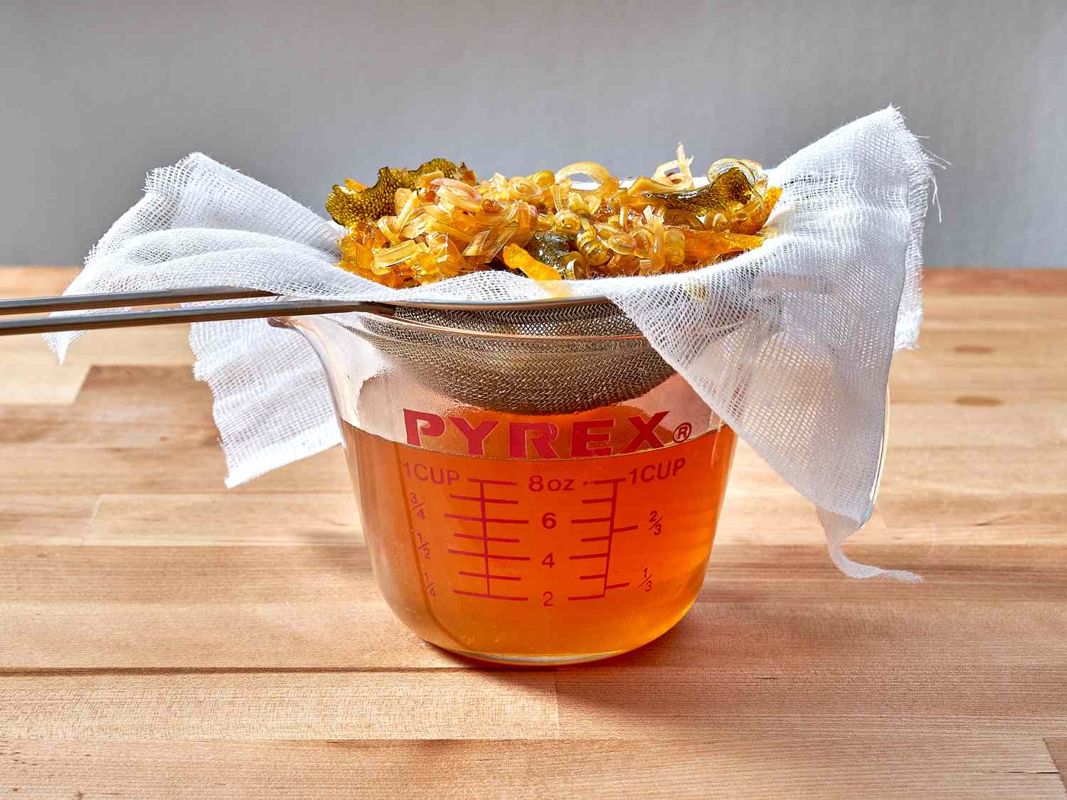 Tonic mixture being strained through cheesecloth and a strainer.