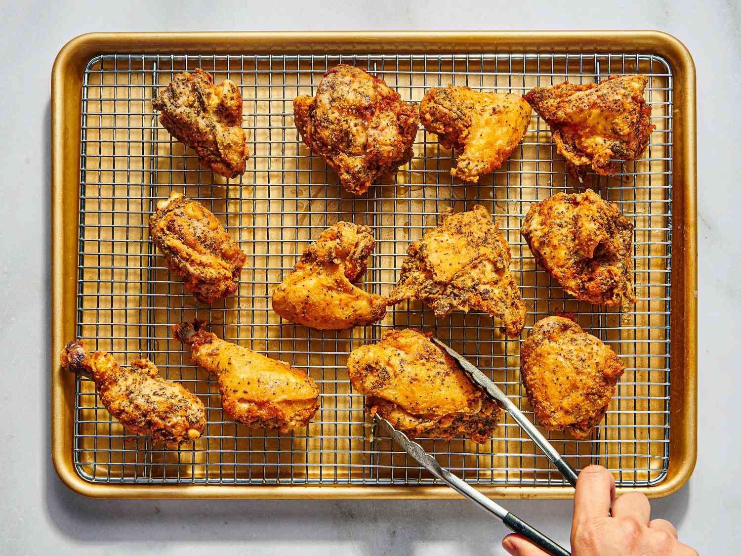 placing chicken on cooling rack on sheetpan with tongs 