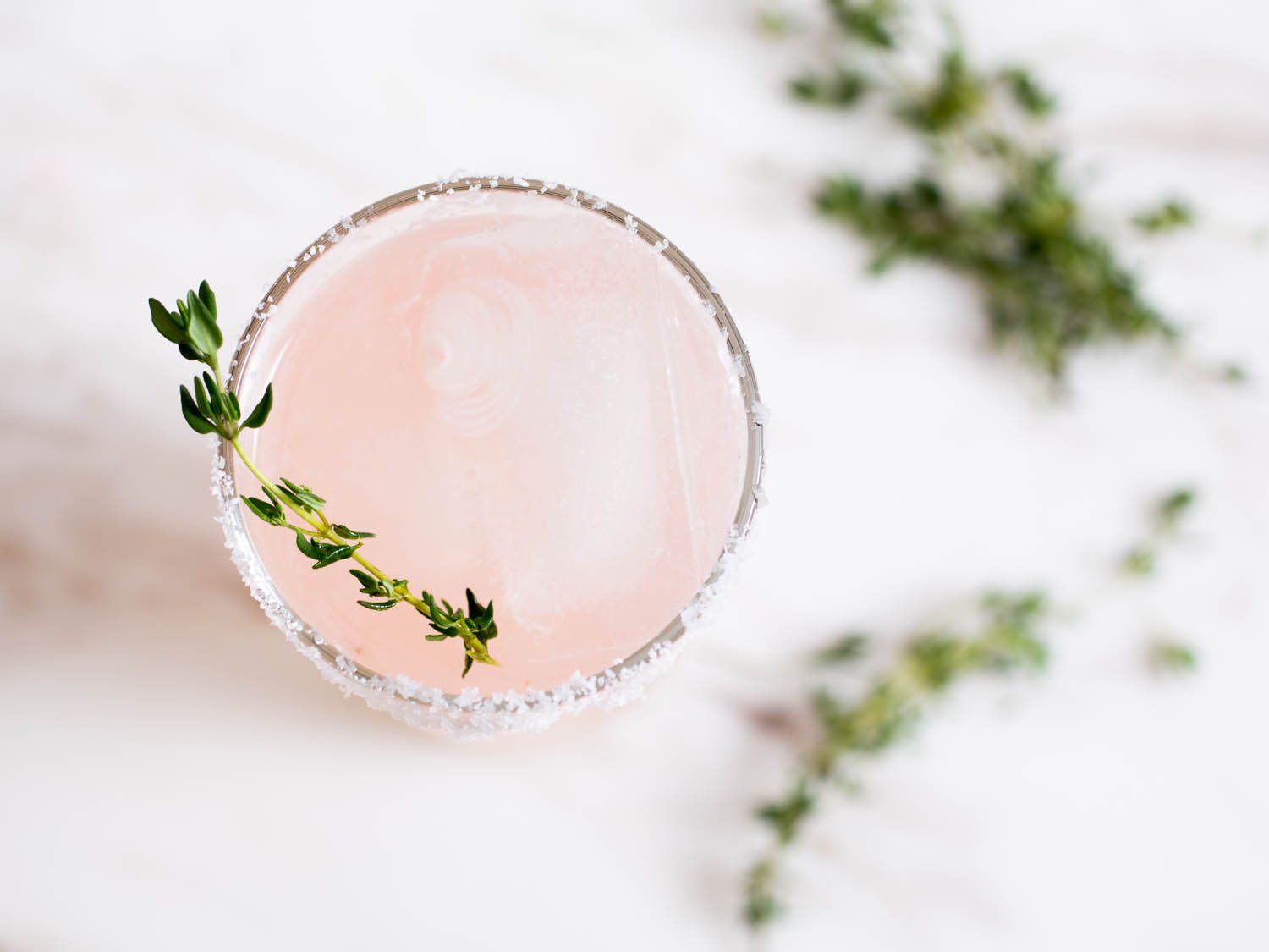 An overhead view of a pretty pink salty dog garnished with fresh thyme.