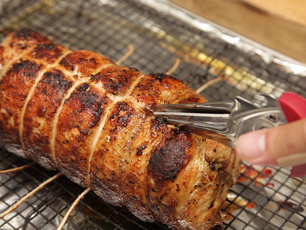 Using kitchen shears to snip off the twine of a roasted turkey porchetta (turchetta) before serving.