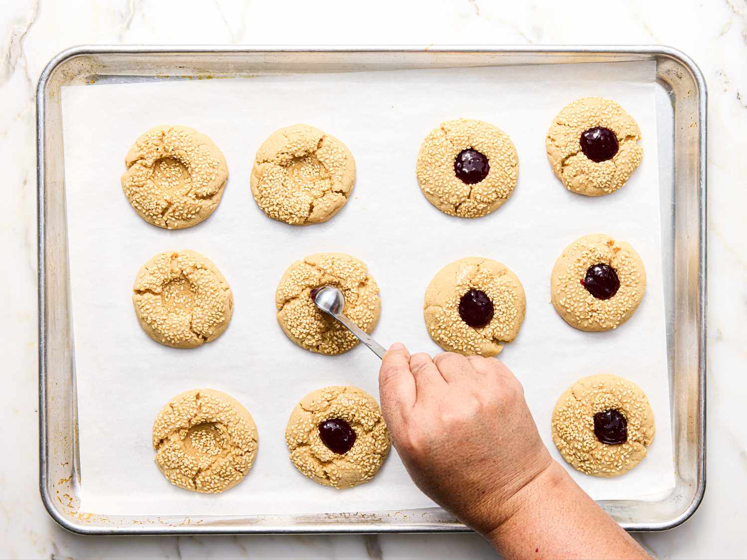Person shaping thumbprint cookies on a tray filled with a raspberry filling