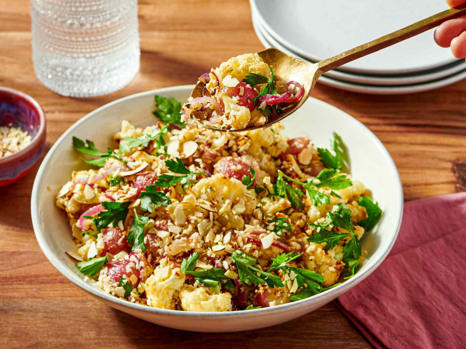 A dish of roasted cauliflower with grapes herbs and nuts being scooped with a spoon