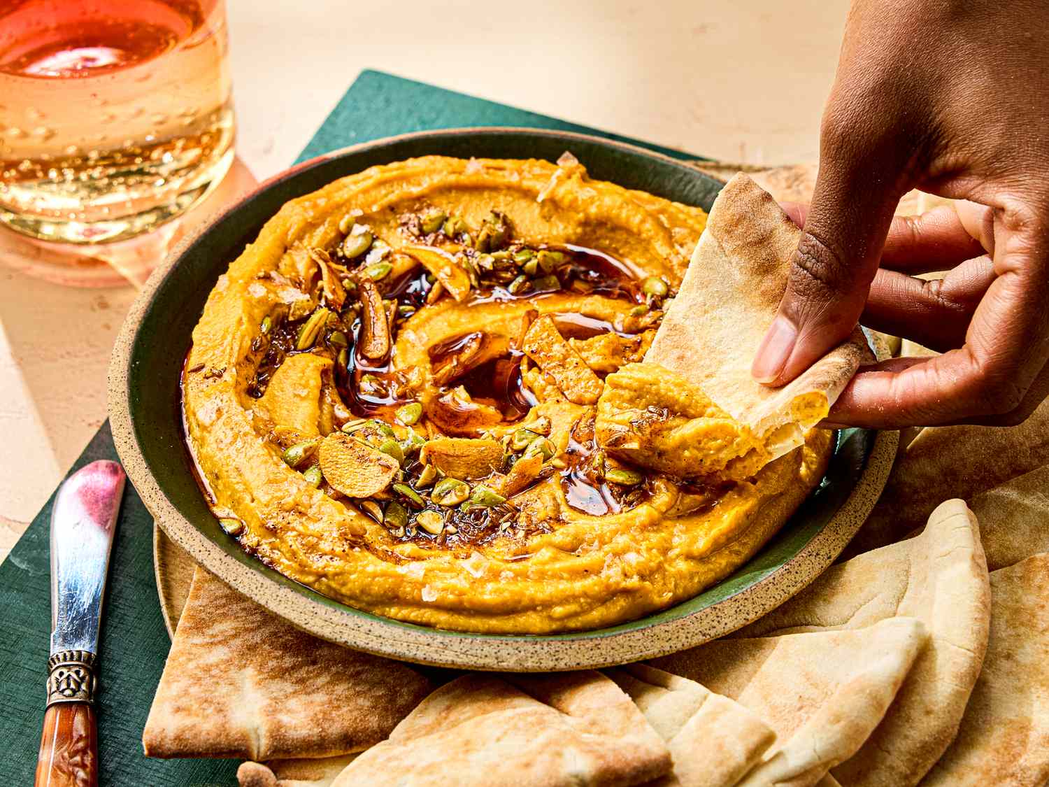 A bowl of sweet potato pepita dip with a person dipping a piece of flatbread
