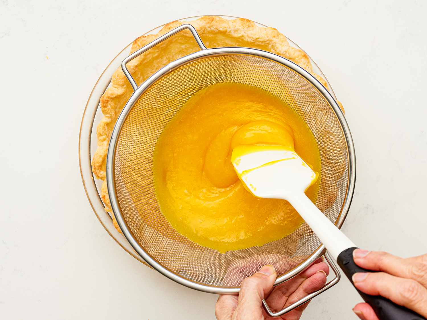 Overhead view of straining mixture into pie curst