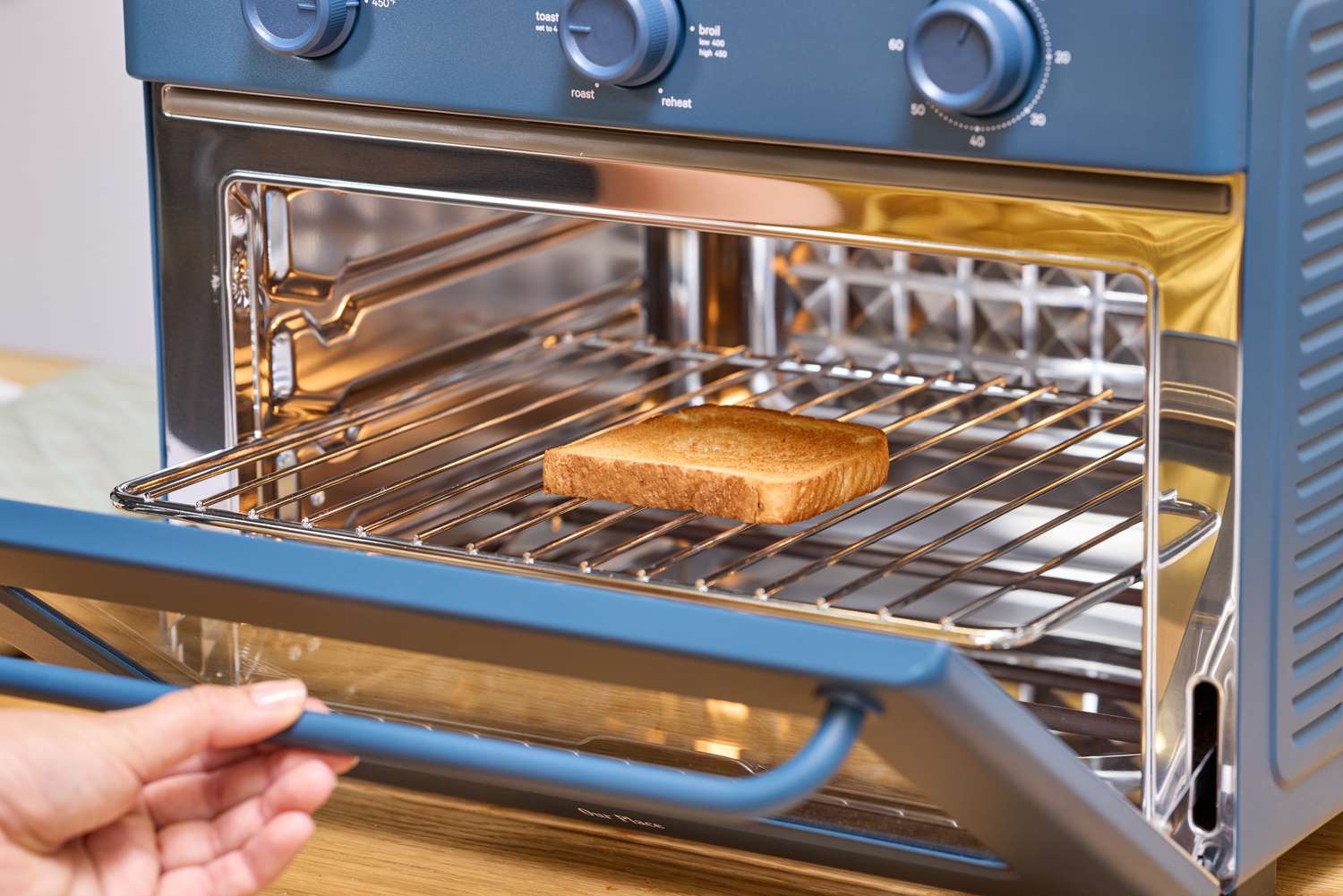 A hand opening the door of the Our Place Large Wonder Oven after toasting bread