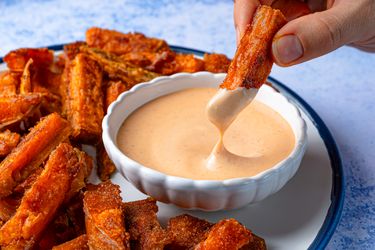 Hand dipping a sweet potato fry into a bowl of sauce sweet potato fries arranged on a plate