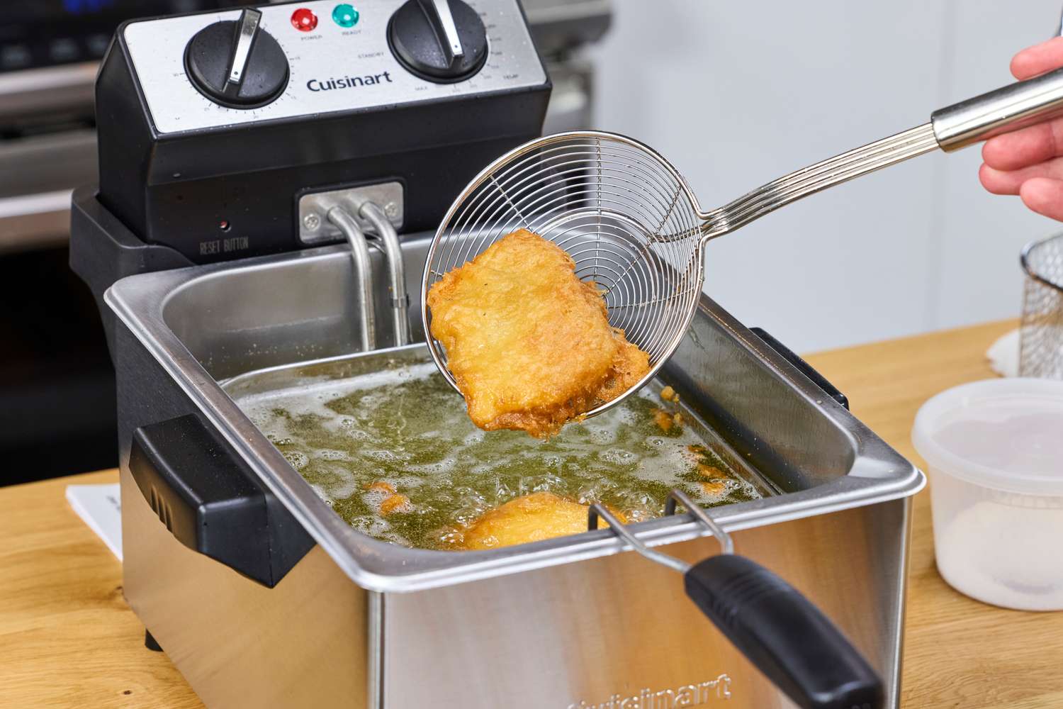 A metal fryer spoon lifting a cooked piece of food out of the Cuisinart CDF-200P1 Deep Fryer