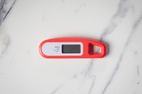 A red thermometer on a marble countertop.