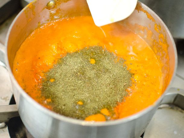 Adding fenugreek to a pot of homemade butter chicken sauce