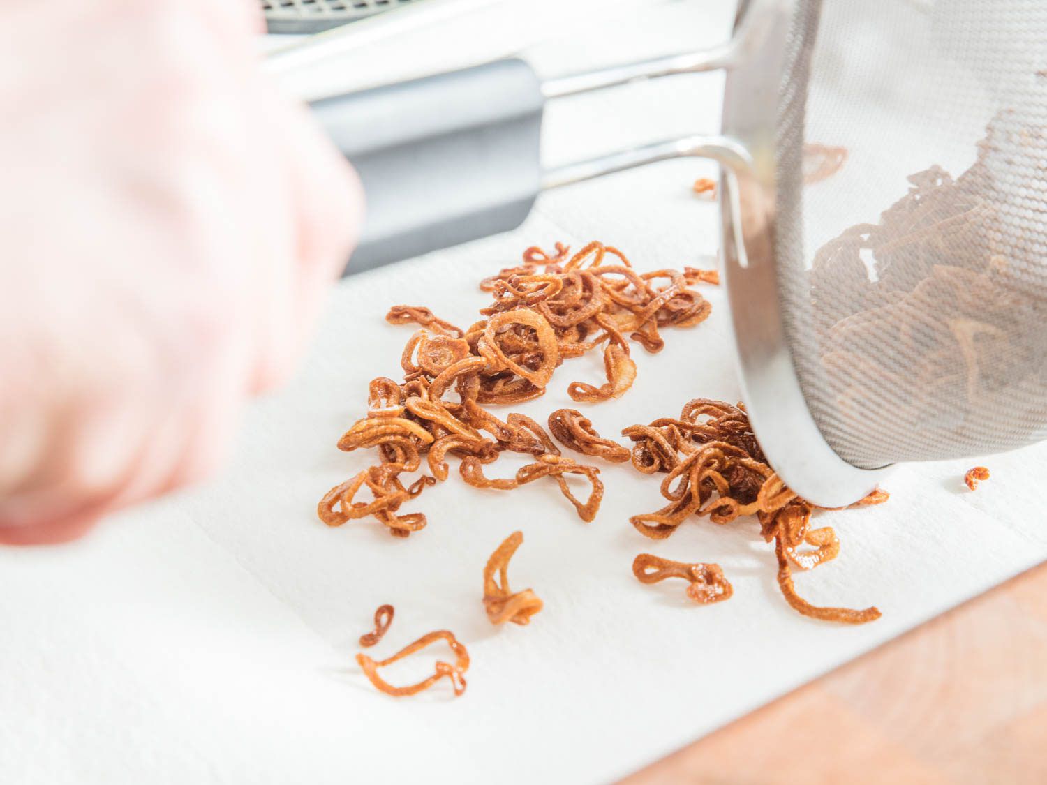 Transferring fried shallots from the fine-mesh strainer to a paper towel-lined baking sheet.