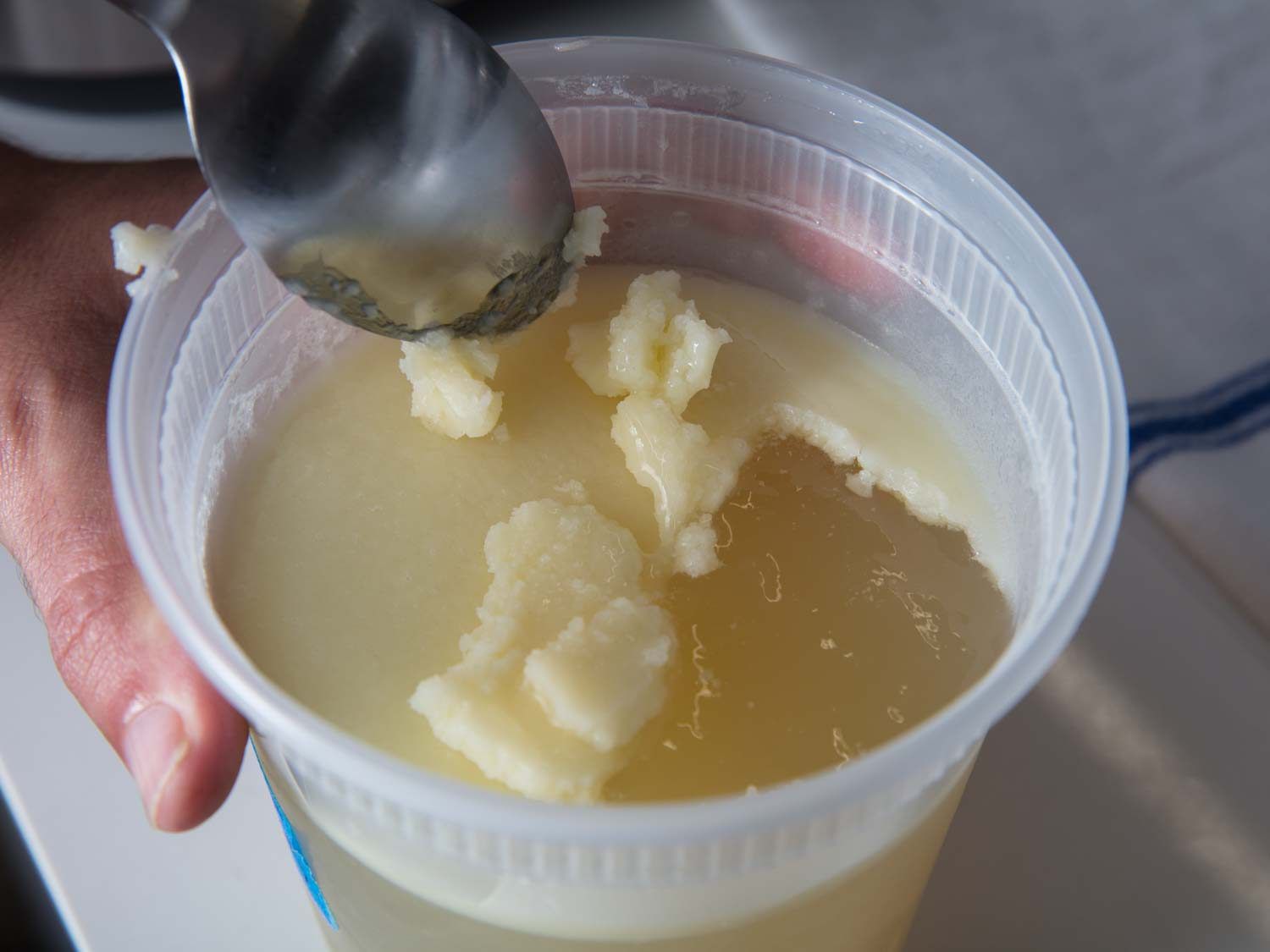Using a spoon to skim hardened fat from an aroma oil for ramen.