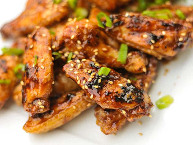 A close-up shot of grilled hoisin-glazed chicken wings sprinkled with sesame seeds and thinly sliced scallions.