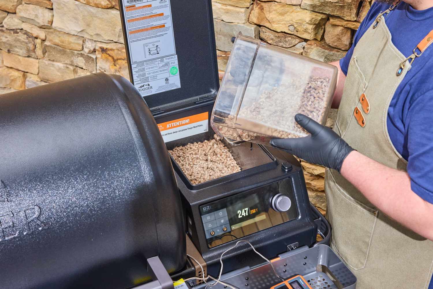 A person adding wood pellets to a Traeger grill
