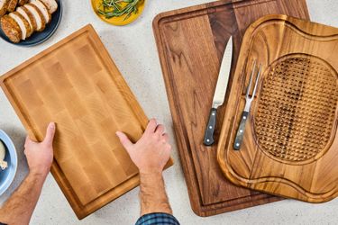 Various wooden carving boards displayed on a table with a persons hands handling one of them accompanied by a plate of food
