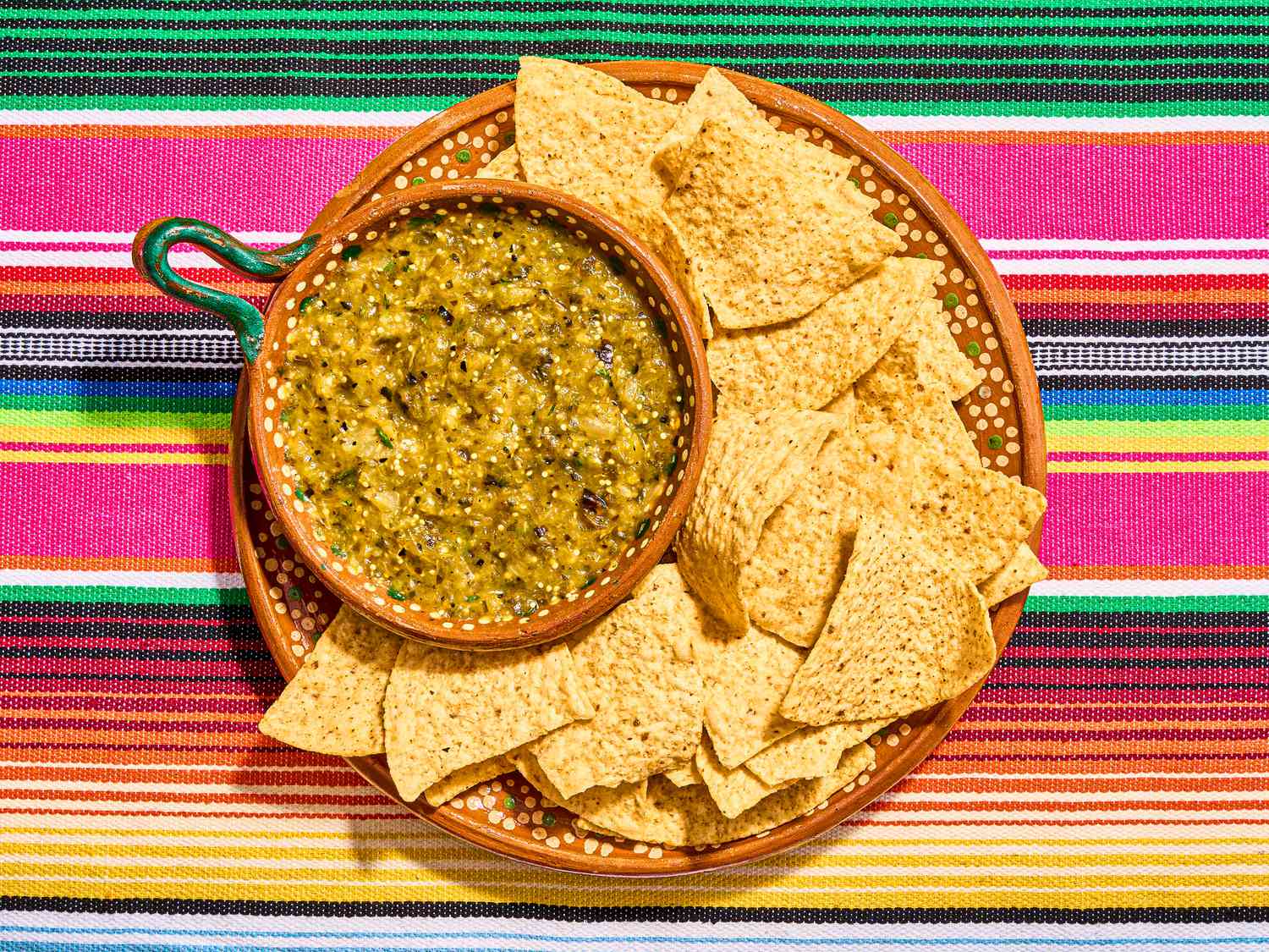Mexican clay bowls with tortilla chips and charred salsa verde on a colorful traditional Mexican textile 