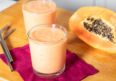 Two glasses of fruit smoothie next to half a papaya on a table