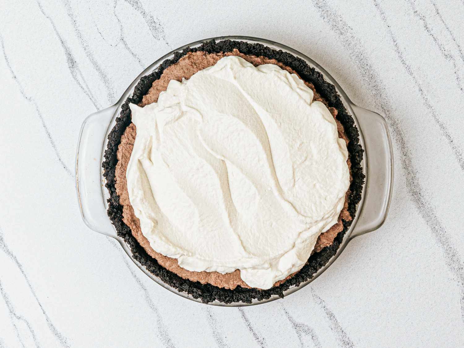 A creamtopped dessert in a round dish with dark crust edges on a marble surface
