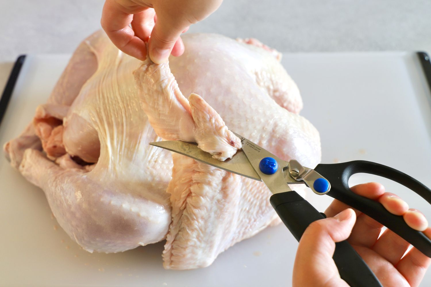 using poultry shears to trim the wing tips of an uncooked roaster