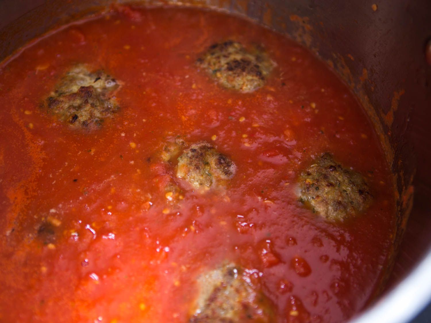 Simmering browned meatballs in tomato sauce.