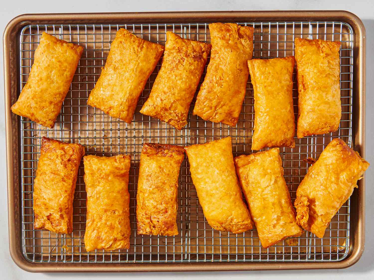 A cooling rack holding several rectangular apple hand pies placed on a baking sheet arranged in neat rows