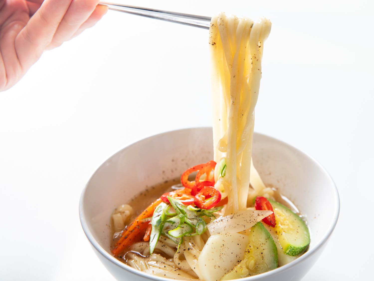 A pair of chopsticks lifts knife-cut noodles from a bowl of Korean knife-cut noodle soup