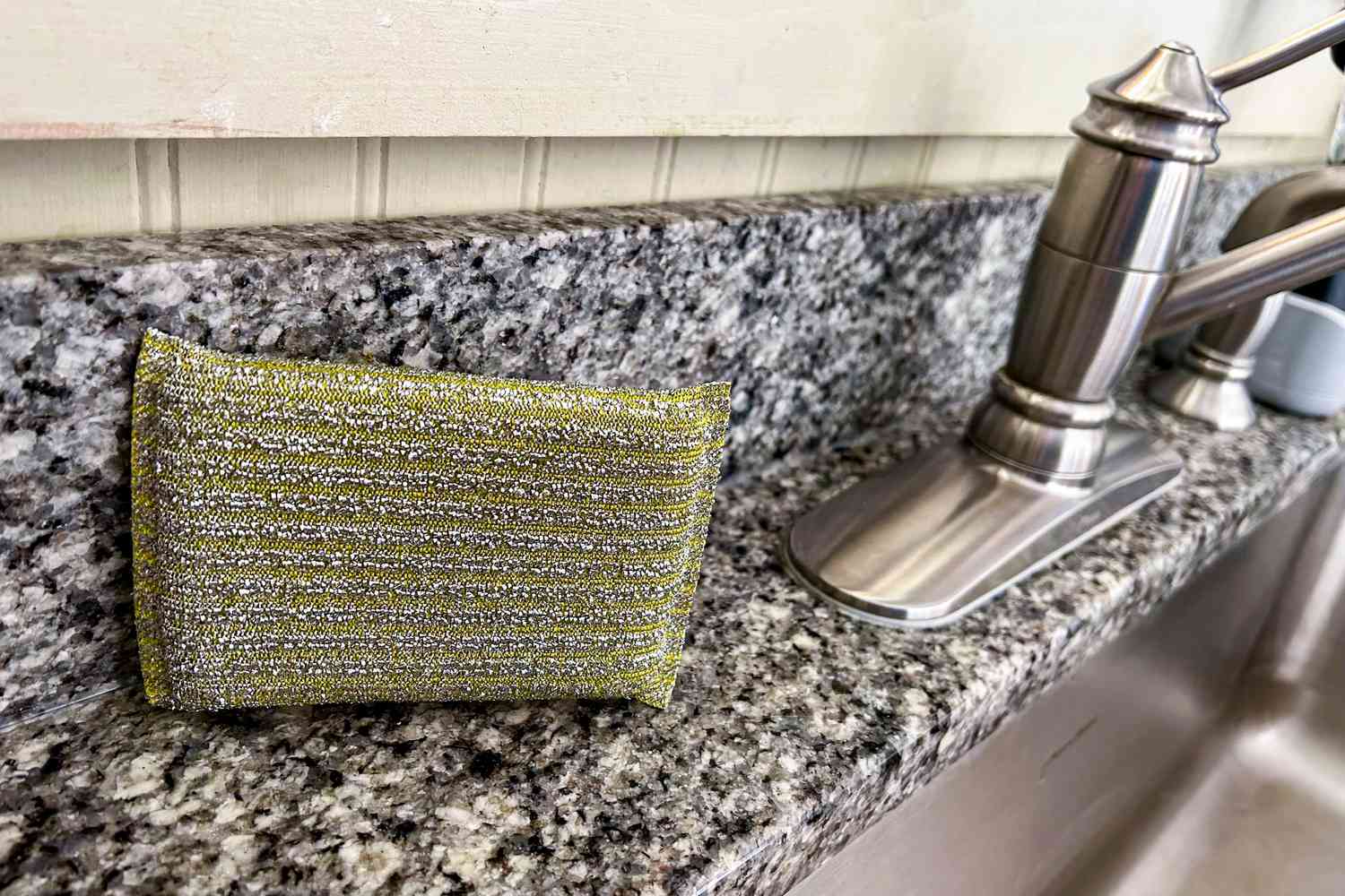 A sparkly gold dishwashing sponge from Hawkins New York next to a kitchen sink