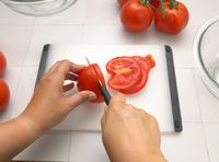 a person slicing a tomato with a paring knife